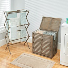 Towels hanging on bamboo collapsable laundry rack, bamboo hamper, gray wall, rug, natural wood floor