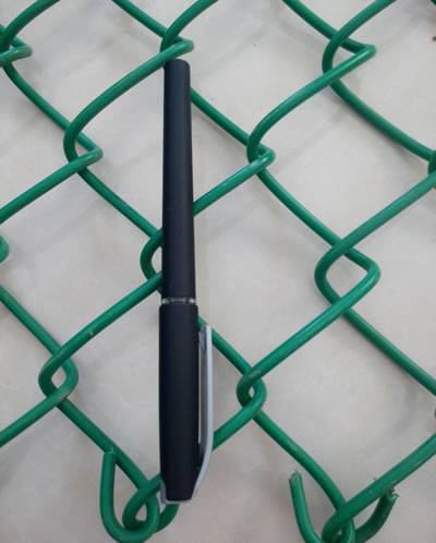 A black pen is placed on green PVC coated chain link fence and two holes' length is equivalent with a pen's length.