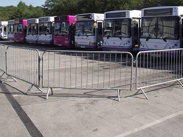 Crowd control barriers are enclosed an area where several bus are parking.