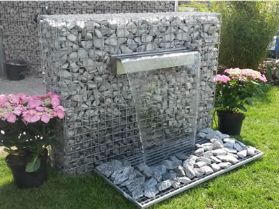 A welded gabion waterfall in the garden with two pot of flowers on the side.