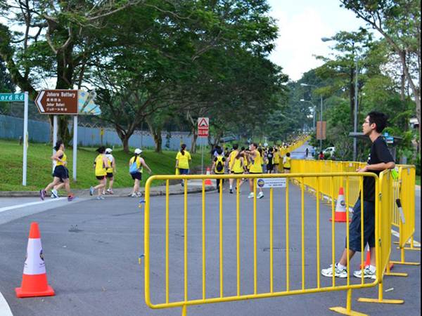 Several runners are running on the road which is enclosed by yellow crowd control barrier.