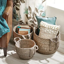 3 natural woven baskets holding throw pillows, books, blanket, teal, brown, cream window curtain